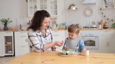 Adorable toddler boy refuses to eat vegetables that his mother offers him. A young mother worries that her son does not want to eat vegetables and tries to persuade him to eat a piece of broccoli.