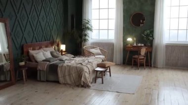 Cozy bedroom interior in boho style with wooden furniture, console table, textiles, green walls, large windows and potted plants. Empty space. High quality FullHD footage