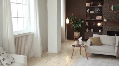 Bej kanepeli, büyük pencereli, kahverengi duvarlı, ahşap zeminli şöminesi kitaplarla, dekorlarla ve saksılarla dolu aynalı şöminesi olan modern tarz ferah oturma odası. Konforlu bir dağ evi..