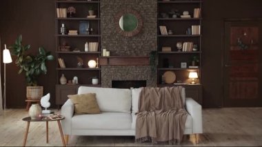 Modern stylish spacious living room with sofa on the background of brown wall with brick fireplace and shelving filled with books, decor and potted plants. Cozy chalet interior. Copy space in the end.
