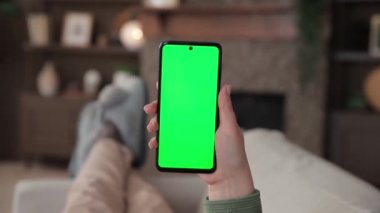 Kanepede uzanmış, krom anahtar yeşil ekranlı akıllı telefon kullanan bir kadının bakış açısı. Chromakey reklam uygulamaları ya da yayın hizmetleri için modelleme yapıyor. Seçici odak.