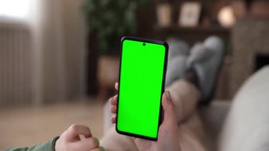 Kanepeye uzanmış, krom tuşlu yeşil ekranlı akıllı telefon kullanan internet ve haberleşme kavramları gibi çeşitli jestler yapan bir kadının bakış açısı..