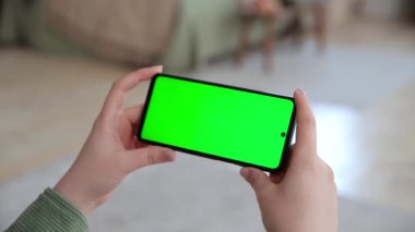 Anahtar yeşil ekranlı, yatay akıllı telefon kullanan kadın elleri görüntüsünü kapat. Chroma tuşu, yayın hizmetleri uygulamaları için bir model oluşturur. İnternette video izliyorum. Seçici odak.