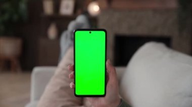 Kanepede uzanmış, krom anahtar yeşil ekranlı akıllı telefon kullanan bir kadının bakış açısı. Chromakey reklam uygulamaları ya da yayın hizmetleri için modelleme yapıyor. Seçici odak.