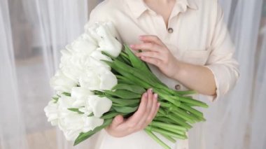 Tanımlanamayan beyaz kadın büyük beyaz laleler tutuyor. Yakından. İlk bahar çiçeklerinin buketi ellerinde. Çiçekçilik ya da çiçek teslimatı konsepti. Sığ dof.