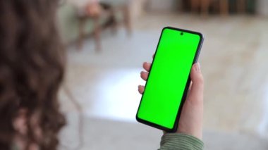 Fotokopi alanı için yeşil ekranlı akıllı telefonu tutan genç bir kadının arka plan görüntüsü. Tap, kaydırma ve kaydırma hareketleri yapıyor. Chroma tuşu reklam ve sosyal ağlar için modelleme yapıyor. İnternetten alışveriş..