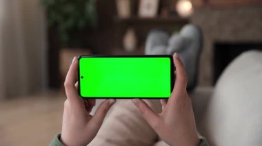 Kadının kanepeye uzanmış yatay akıllı telefon ve yeşil ekran krom anahtar kullandığına dair bakış açısı. Chromakey reklam uygulamaları ya da yayın hizmetleri için modelleme yapıyor. Seçici odak.