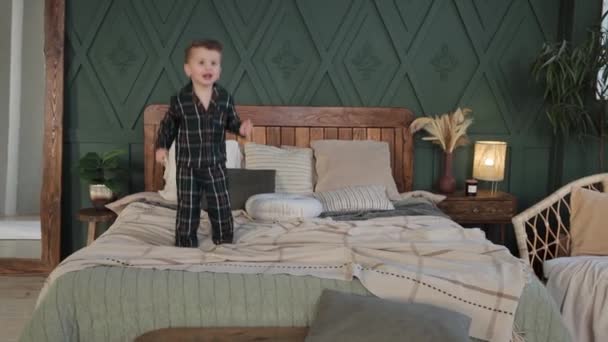 パジャマ姿のかわいい白人の幼児の男の子がスキップし 居心地の良いスタイリッシュなベッドルームで目を覚ました後 両親のベッドの上で高くジャンプします 幸せな子供は楽しんでいます 子供じみたな 朝の演習 — ストック動画