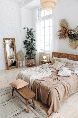 Boho etnik dekoru olan rahat kırsal yatak odası. Geniş pencereli, ferah bir daire. Tahta mobilyalar. Büyük ayna. El yapımı tekstil. İç kısımda bitkiler var. Kimse..