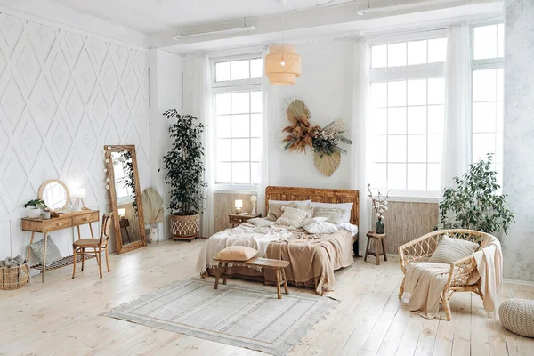 Boho etnik dekoru olan rahat kırsal yatak odası. Geniş pencereli, ferah bir daire. Hiç kimse. Tahta mobilyalar. Yatak odası masası. Büyük ayna. El yapımı tekstil. İç kısımdaki bitkiler..