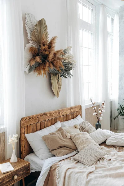 stock image Cozy rustic bedroom with boho ethnic decor. Large windows. Double wooden bed with many pillows and handmade textiles. Wooden furniture. Nobody. Large windows in appartment.