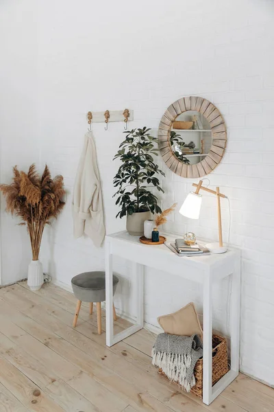 Console table with a potted plant, a table lamp and a round mirror in a wooden frame in a modern stylish living room in a Scandinavian style. Nobody.