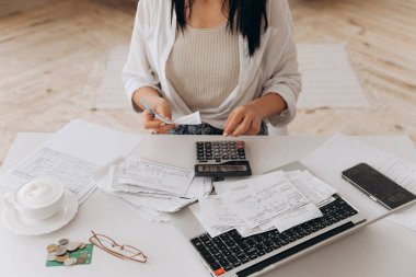 Beyaz ofis masasında finans kağıtlarıyla çalışan, faturaları ödeyen, hesap makinesine güvenen, para biriktirmek için bütçe planlayan bir kadının üst görüntüsü. Bağımsız muhasebe, uzak muhasebeci.