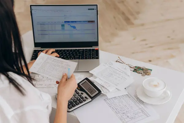 Tanınmayan kadının arka görünümü dizüstü bilgisayar ve hesap makinesindeki kamu giderlerini hesaplar, çevrimiçi fatura ödemeleri ve mali belgeler hazırlar, finansal tavsiye kavramı ve uzak çalışma platformları.