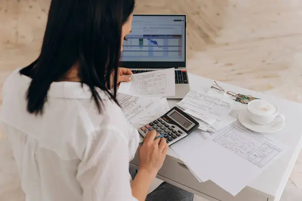 Esmer kadının arka planı dizüstü bilgisayar ve hesap makinesindeki kamu giderlerini hesaplar, çevrimiçi fatura ödemeleri ve mali belgelerle ilgilenir, finansal tavsiye kavramı ve uzak çalışma platformları.