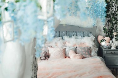 Pastel pembe yatak odası, yumuşak yastıklar ve oyuncak ayı. Bulanık beyaz ağaçtan mavi çiçekli ve fenerli görüntüler, sihirli bir dokunuş ekliyor. Ev dekorasyonu ve iç tasarım için uygun.