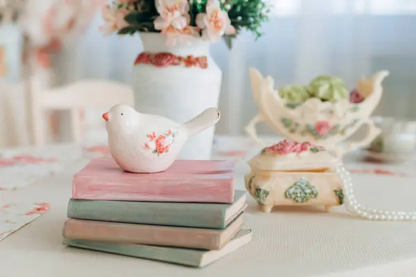 stock image Charming scene with a ceramic bird on stacked pastel books, floral accents, and a vintage vase. The composition exudes a cozy, elegant, and peaceful atmosphere, perfect for a rustic setting.