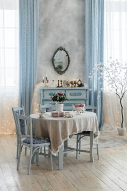 Dantel masa örtüsü, mavi sandalyeler ve çiçek desenli masa örtüsü olan çok güzel dekore edilmiş yemek odası. Antika elbise ve ayna odaları güzelleştirir..