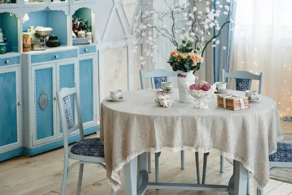 Pastel mavi mobilyaları, zarif masa dekorları ve çiçek dekoru olan büyüleyici bir iç mekan. Dantelli masa örtüsü ve antika çay fincanları biraz sofistike ve klasik çekicilik katar..