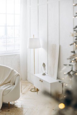 Modern bir zemin lambası, küçük beyaz bir dolabı ve şenlikli dekoru olan zarif ve parlak bir oda köşesi. Noel ağacı dikizleyip sıcak bir tatil ortamı yaratıyor..