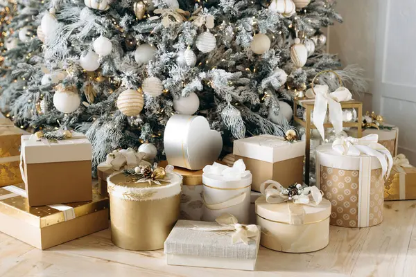 Güzel süslenmiş bir ağacın altında altın ve beyaza sarılmış Noel hediyelerinin yakın çekimi. Dekoratif yay ve süsler biraz zarafet katar. Ilık ışıklandırma rahat bir tatil ortamı yaratır.