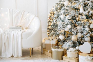 Battaniyeye sarılı beyaz kanepeli rahat bir tatil odası, ışıklarla ve süslerle süslenmiş Noel ağacı, altın ve beyaz hediye kutuları, şenlikli bir ortam..