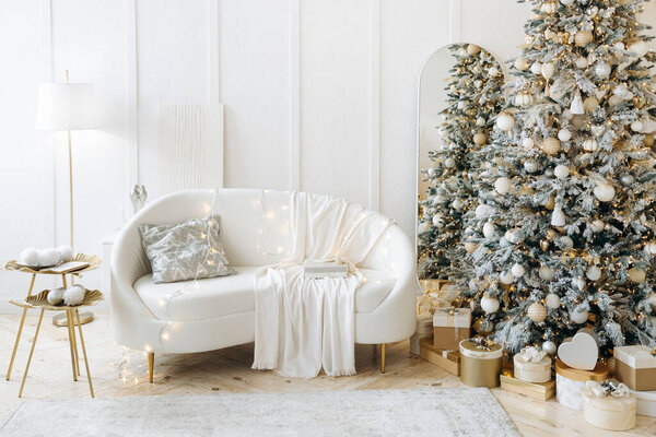 Элегантная гостиная, оформленная на Рождество, белый диван с декоративными огнями и одеялом, елка с орнаментами и подарочными коробками, золотые столы, лестница, праздничный и стильный.