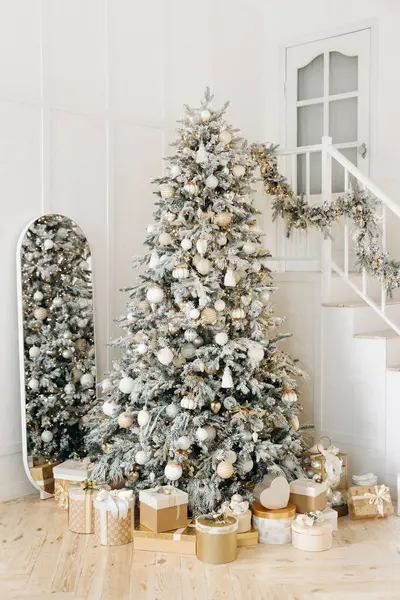 Süslü bir ağacı olan şık bir Noel kurgusu ve merdivenlerin altında altın ve beyaz hediyeler. Merdivenlerdeki çelenk ve ayna şenlik cazibesini artırıyor..