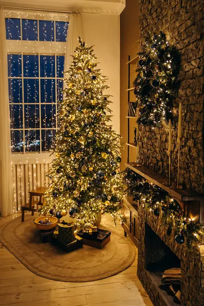 Büyük bir penceresi, yeni yıl çelengi ve hediyeleri olan bir şöminesi olan rahat bir odada birçok çelenkle süslenmiş Noel ağacı. Noel arifesi. Akşam Yeni Yıl Büyüsü.