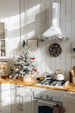 Tezgahın üzerinde kırmızı ve beyaz süslemeli buzlu bir Noel ağacı, şenlikli bir çelenk ve çeşitli mutfak eşyalarının yer aldığı güneşli bir mutfak sıcak bir tatil atmosferi yaratıyor..