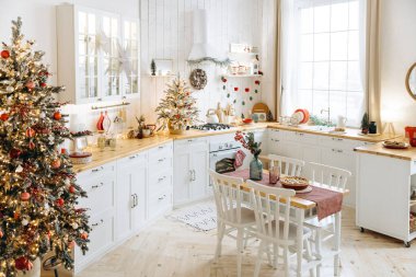 Festive kitchen decorated for Christmas with frosted trees, red and white ornaments, white cabinets, holiday decorations, and a dining table set with a pie, creating a cozy and cheerful atmosphere. clipart