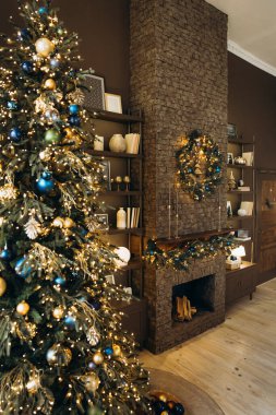 Süslü bir Noel ağacının olduğu tipik bir Noel sahnesi. Işıklı, şenlikli bir çelenk ve çelenkli taş bir şömine. Dekorla dolu raflar rahat atmosferi güçlendirir.