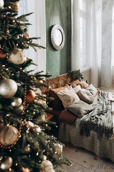 Büyük çift kişilik bir yatakta, yeşil duvarları ve güneş ışığıyla dolu büyük pencereleri olan geniş bir yatak odasının ahşap yatak başlığıyla bir Noel ağacının içinden bakın. Sıcak ve neşeli bir atmosfer..