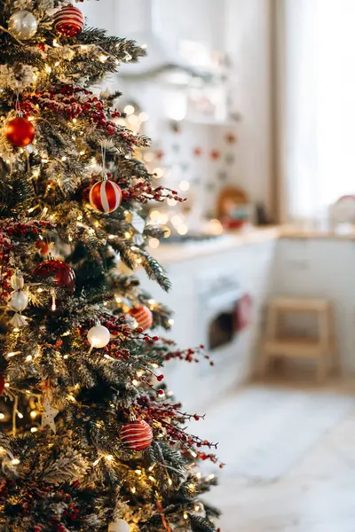 Kırmızı ve beyaz takılar, ışıklar ve böğürtlenlerle süslenmiş Noel ağacı. Mavi arka planda sıcak bir mutfak ve sıcak tatil havası var. Sığ DOF.