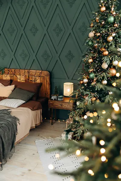 Noel için dekore edilmiş yatak odası. Yatak odasının içinde zümrüt ve bronz toplarla süslenmiş yeşil Noel ağacı var. Çelenk ışıklarındaki bulanık Bokeh 'e bak. Noel arifesi. Kimse..