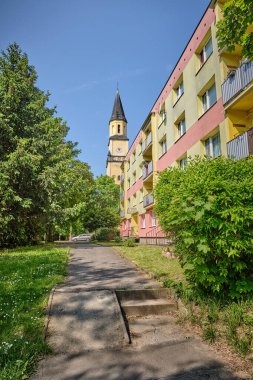 Eski asfalt park yolu termal yalıtımlı apartman blokları, ağaçlar, yeşil çimenler. Arka planda kilise ve araba var. Doğu Avrupa 'da küçük bir kasabanın yerleşim alanı. 