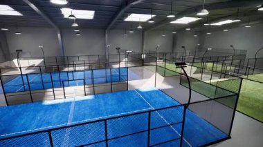 Spor tesisi bölgesinde bulunan bir depo binasının içindeki boş yeşil ve mavi padel tenis kortlarının insansız hava aracı görüntüsü. Gündüz aydınlatma armatürleri aydınlatılmış