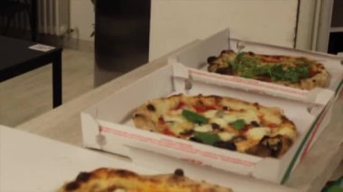 Set of freshly baked pizzas and in final preparation stage. Neapolitan pizzas with high crust. Workers dressing in pizzeria.