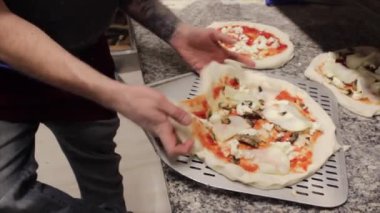 Pizza maker at work while he bakes the pizzas with a special shovel in a wood-burning oven for cooking. Spreading technique with flour on a marble pizza counter. Video of professional at work.