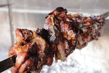 Circular photo. Grilled lamb and goat meat skewer. Cooked with wood fire. Brazilian-style churrasco. Spinning spit. Medium cooked roasted meat.