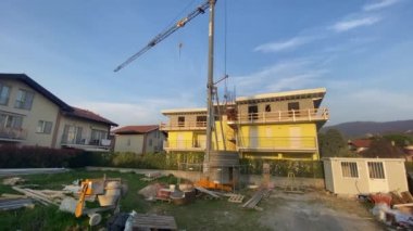 Ön planda ağır demir vinç bulunan yapım aşamasındaki ev. İnşaat devam ediyor. Çalışmalar devam ediyor. İnşaat alanı açıldı.