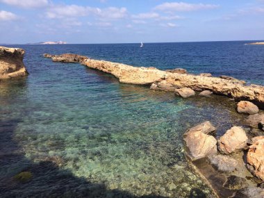 Ardıç ve şemsiye ağaçlarından oluşan alçak bir orman. Insular Akdeniz maketi. Girintili ve kesintisiz kıyı şeridi. Kayalar sığ sularla dolu sakin bir denize battı..