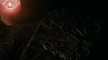 Book of black magic with the eye symbol and the burning candle on side. Close-up.