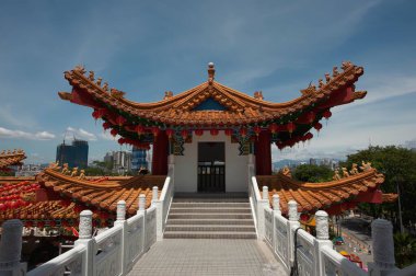 Geleneksel bir Çin binasının çatısını süsleyen altın bir ejderha heykelinin canlı görüntüsü açık mavi gökyüzüne karşı kırmızı fenerlerle bezenmiş..