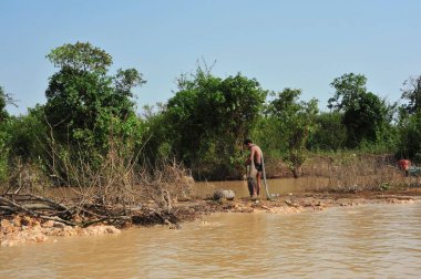 Siem Reap Angkor Wat Kamboçya 'daki bir ağacın yanında bir adam duruyor. Su kahverengi ve bulanık. Adam siyah bir gömlek ve şort giyiyor.