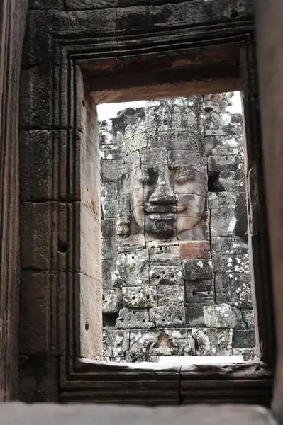 Stock image View of a serene ancient stone face sculpture at Angkor Wat, Cambodia, seen through a stone window, evoking mystery and history in Siem Reap.