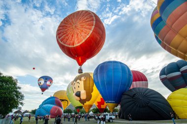 Sıcak hava balonu festivalini izlemek için büyük bir kalabalık toplandı. Bir sürü farklı renkli balon var, turuncu şeklinde kırmızı balon ve aslan şeklinde mavi balon da dahil.