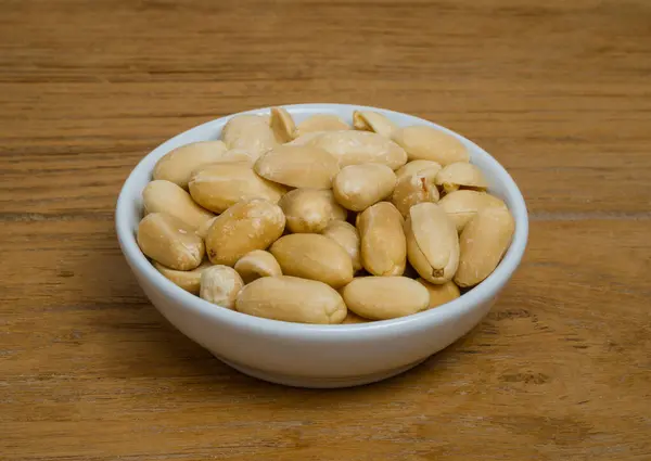 Small bowl of roasted salted peanuts isolated on wooden background.