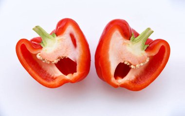 Beyaz arka planda iki parça kırmızı biber izole edilmiş. Taze olgun kırmızı biber dilimlenmiş. Üst Manzara. Bahçedeki sağlıklı yiyeceklerin parlak renkleri. 