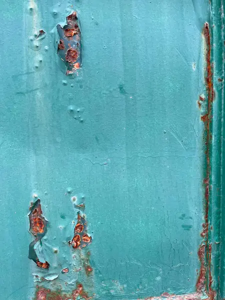 Abstract grunge background texture, closeup of old greenish-blue metal door or wall. Peeling paint, white patina, scratches, rusty holes, dents, and cracks. Weather and corrosion marks on aged surface